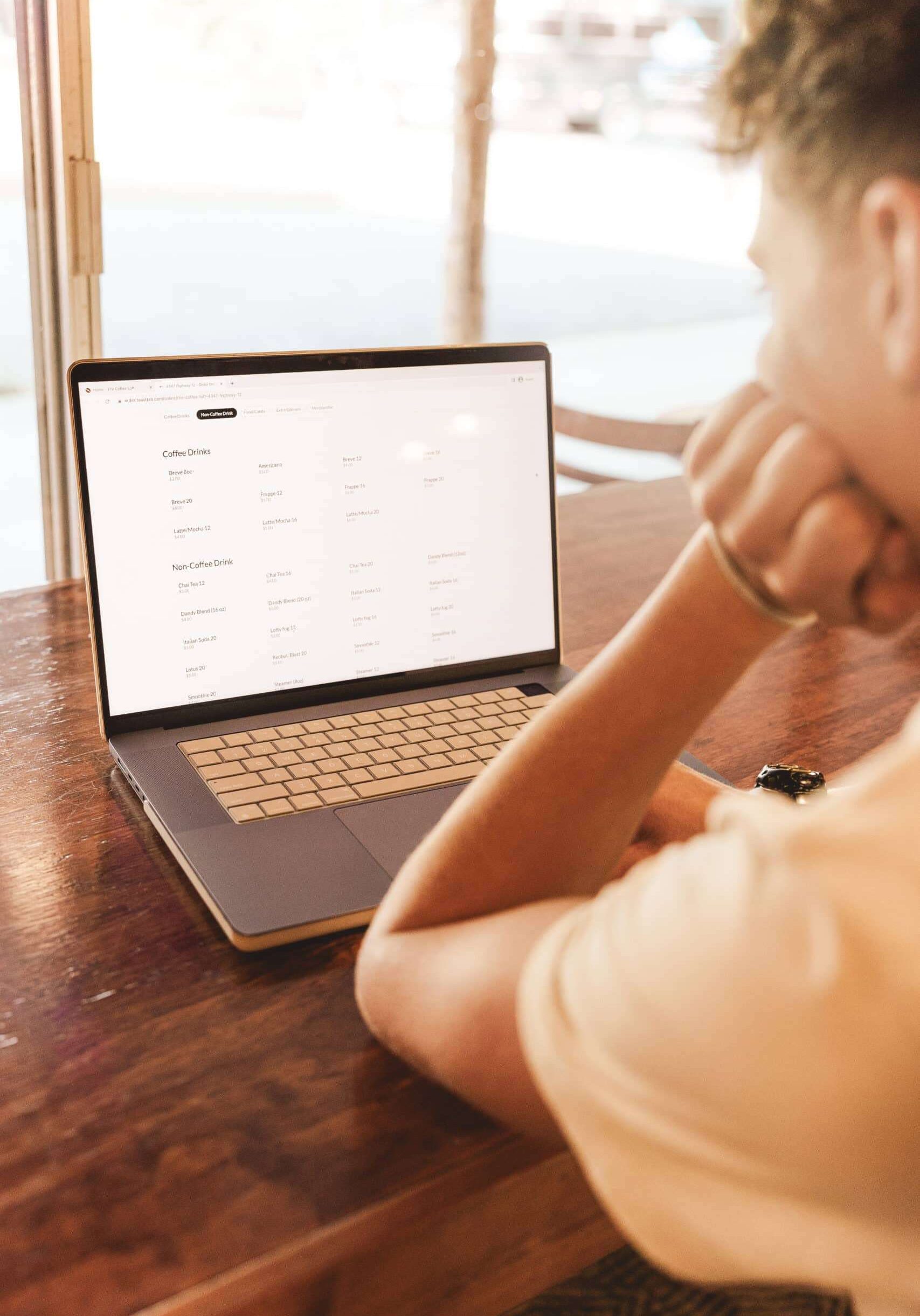 A man sitting in front of a laptop looking at the coffee loft menu on the website